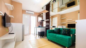 A modern hotel room with a green sofa, a flat-screen TV, a desk, and a glass partition. - Luxurious Bassura City Apartment with Mall Access (Jakarta)