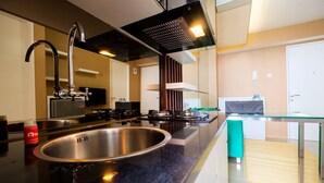 A modern kitchen with a stainless steel sink, a gas stove, and a glass countertop. - Luxurious Bassura City Apartment with Mall Access (Jakarta)