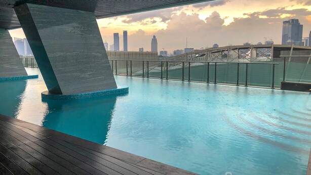 Una piscina interior con vistas a un horizonte urbano, una terraza de madera y una barandilla metálica.