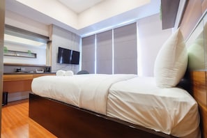 Et moderne hotelværelse med en stor seng, et fladskærms-tv på væggen, et træskrivebord og et vindue med rullegardiner.