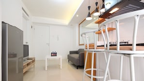 A modern kitchen with a refrigerator, a coffee machine, and a dining area with white bar stools. - Compact Bassura City Apartment near Jatinegara (Jakarta)
