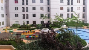 A multi-story residential building with balconies, a children's play area with colorful equipment, and a swimming pool. - Compact Bassura City Apartment near Jatinegara (Jakarta)