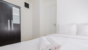 A hotel room with a bed, white linens, a dark wooden wardrobe, and a white door. - Compact Bassura City Apartment near Jatinegara (Jakarta)