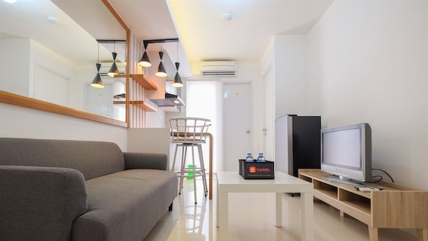 A modern living room with a grey sofa, a white coffee table, a TV on a wooden stand, and pendant lights. - Compact Bassura City Apartment near Jatinegara (Jakarta)