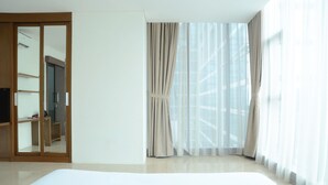 Hotelkamer met een groot bed, een kledingkast en uitzicht op een gebouw door dunne gordijnen.