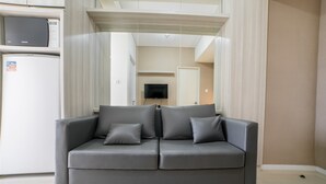 A modern living room with a grey sofa, a flat-screen TV, and a microwave above a white refrigerator.