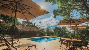 Eine Holzterrasse mit Pool, Liegestühlen und Sonnenschirmen.