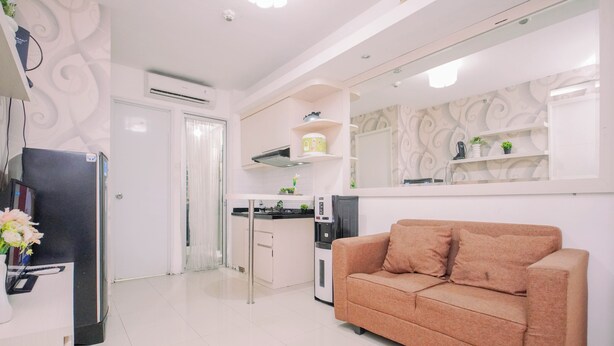 A modern living room with a sofa, a kitchen area with a refrigerator, and a water dispenser. - Exquisite Bassura City Apartment near Shopping Mall (Jakarta)