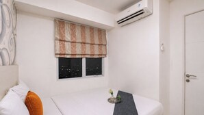 A hotel room with a bed, a window with a view of the city at night, a door, and an air conditioning unit. - Exquisite Bassura City Apartment near Shopping Mall (Jakarta)