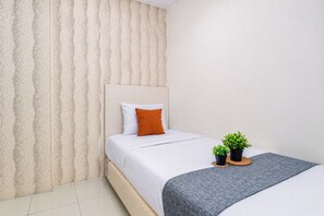 Habitación de hotel con cama, cabecera, manta gris, dos plantas en macetas y pared con textura.