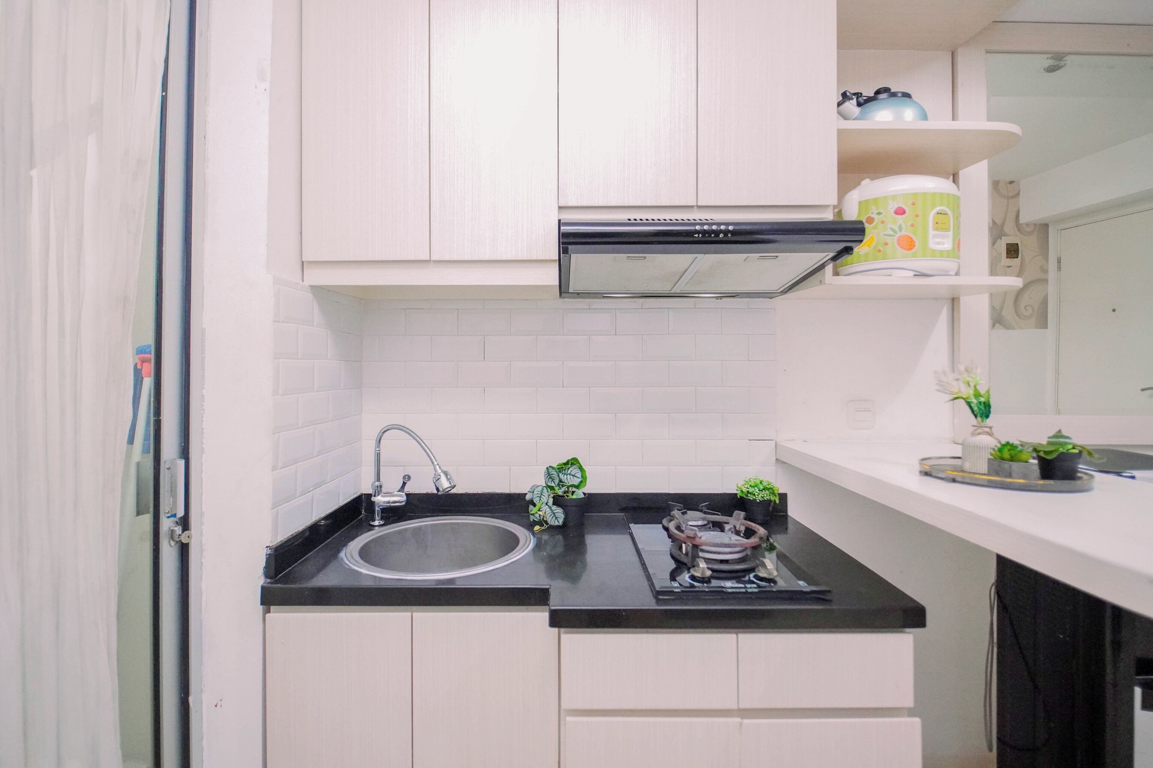 Cocina compacta con pileta de acero inoxidable, estufa a gas y muebles bajos blancos.