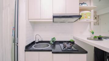 Cocina compacta con pileta de acero inoxidable, estufa a gas y muebles bajos blancos.