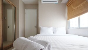 Una camera d'albergo con un letto, un asciugamano bianco arrotolato, un armadio, una porta e una finestra con una persiana marrone.