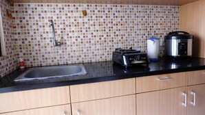 A kitchen with a tiled backsplash, a sink, a toaster, a rice cooker, and wooden cabinets. - Chrysant Kebagusan City Near Cilandak Mall (Jakarta)