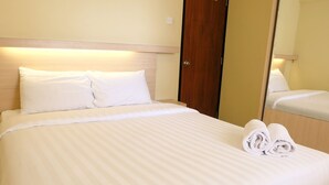 A neatly made bed with white linens and two pillows, a wooden headboard, and a wooden door in the background. - Chrysant Kebagusan City Near Cilandak Mall (Jakarta)