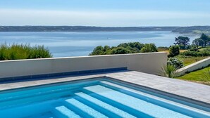 Una piscina con acqua cristallina, circondata da un muretto basso e vista su un'ampia distesa d'acqua e colline lontane.