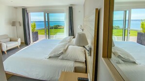 Camera d'albergo con un letto grande, una sedia, una scrivania e vista sul mare.