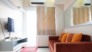Un salon moderne doté d’un téléviseur à écran plat, d’un canapé avec des coussins orange, d’un grand miroir et d’une porte-fenêtre coulissante agrémentée de rideaux à motifs.