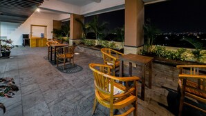 An outdoor patio area with wooden furniture and plants, overlooking a cityscape at night. - Best Price Tamansari Panoramic Apartment with Mountain View (Bandung)