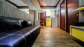 A hotel room with a leather sofa, wooden flooring, a kitchenette, and a door leading to a bathroom. - Best Price Tamansari Panoramic Apartment with Mountain View (Bandung)