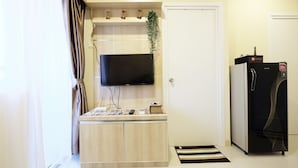 Ein kompakter Wohnraum mit Flachbildfernseher an der Wand, einem kleinen Holzkabinett darunter, einem Kühlschrank und einer Tür mit einem Reise-Hinweisschild.