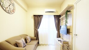 Ein Wohnzimmer mit einer Couch, einem Flachbildfernseher, einer Zieruhr und einer Klimaanlage.