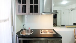 Cozinha compacta com pia de aço inoxidável, fogão por indução dupla e coifa moderna.
