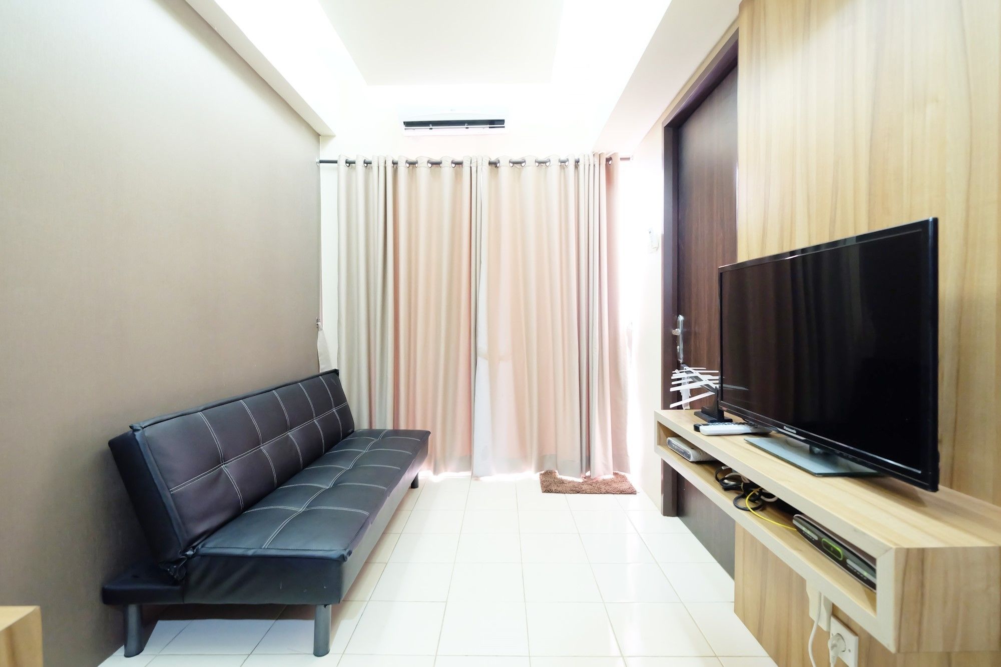 A modern living room with a black sofa, a flat-screen TV on a wooden stand, and a large window with curtains.
