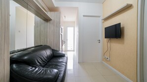 A hallway with a black leather sofa, a mounted TV, and a wooden accent wall. - Modern Apartment Near Cihampelas at Parahyangan Residence (Bandung)