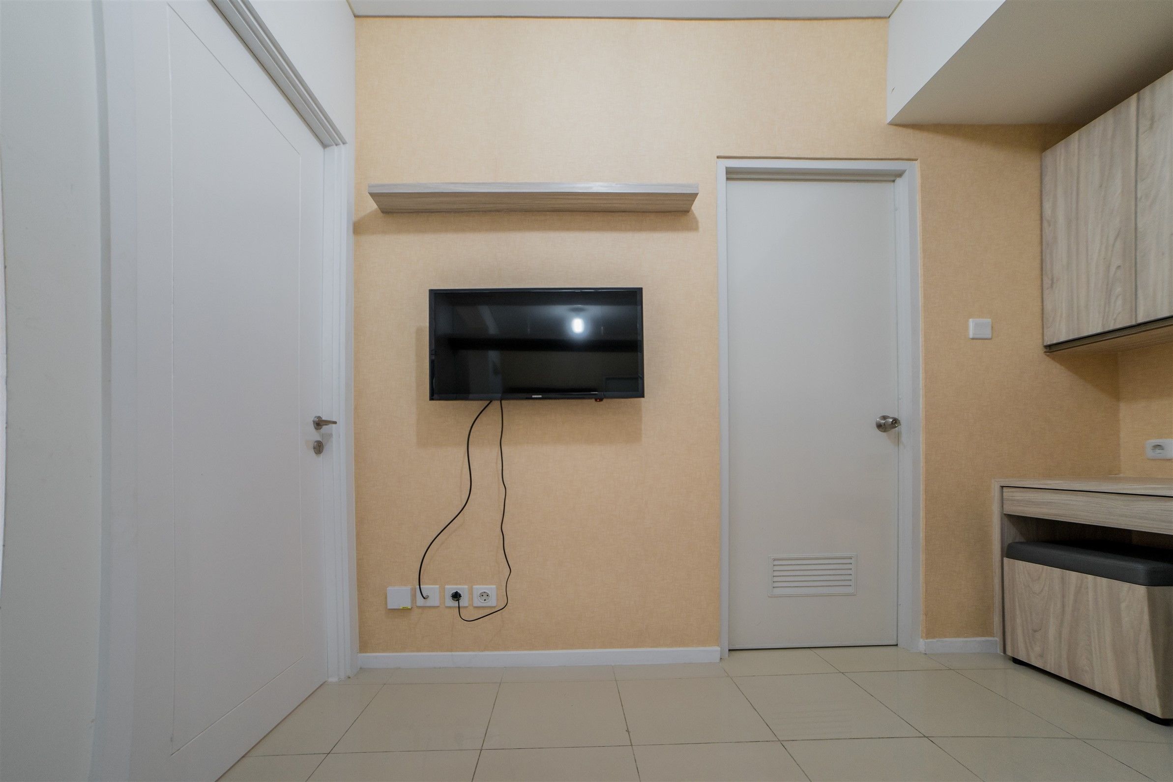 A room with a TV mounted on the wall, a door, and a cabinet.