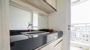 A modern kitchen with a black countertop, stainless steel sink, and a window overlooking a balcony. - Modern Apartment Near Cihampelas at Parahyangan Residence (Bandung)