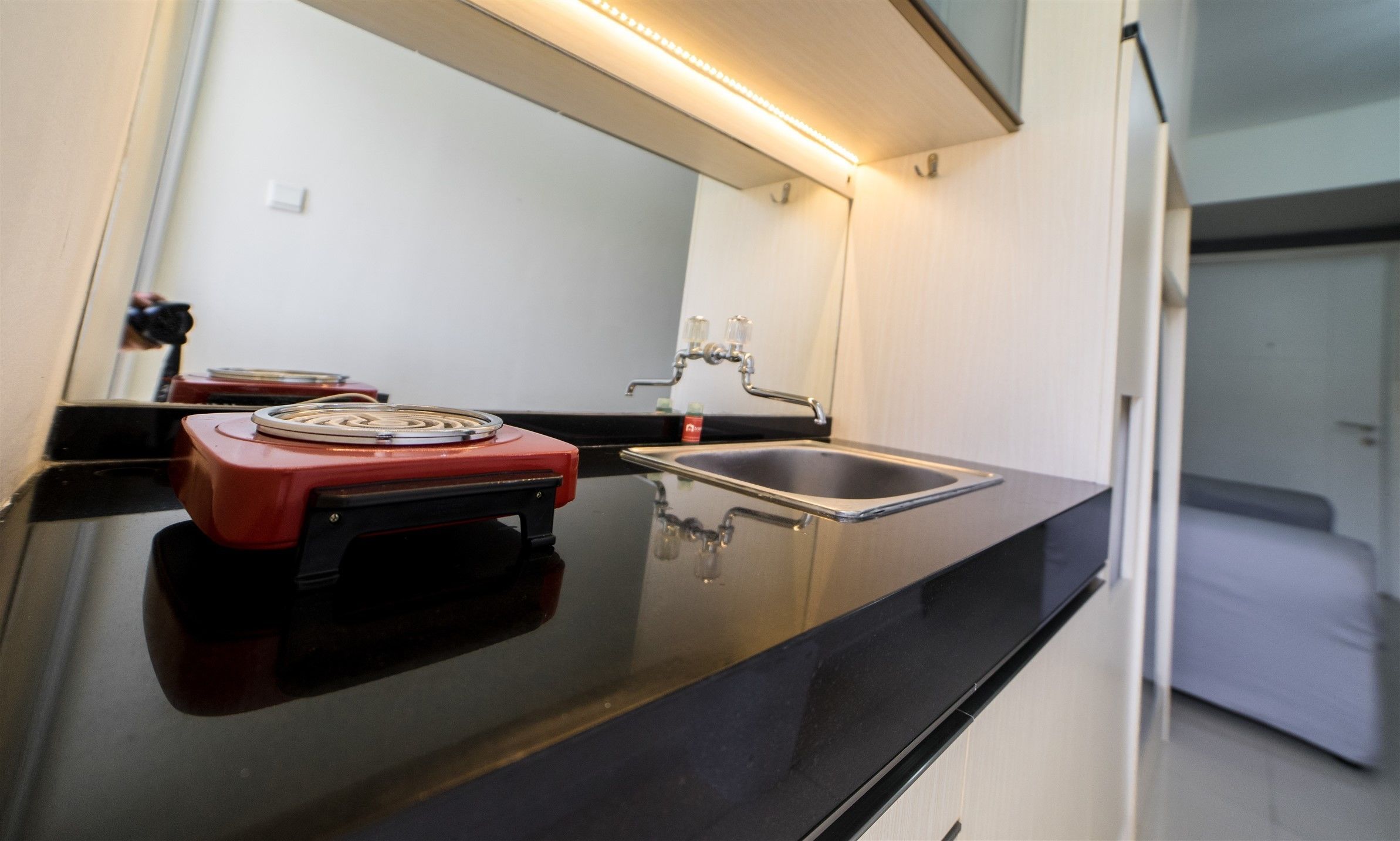 A modern kitchen with a black countertop, a red appliance, a stainless steel sink, and a mirror above the sink.