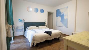 Une chambre à coucher avec un lit, des tables de chevet, un bureau et un tableau représentant des nuages accroché au mur.