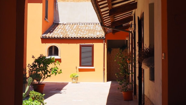 An arched corridor with a tiled roof, potted plants, and a bench. - Giardino 34 (Forlì)