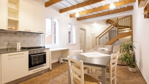 A kitchen with white cabinets, a stove, and a dining area with a table and chairs. - Giardino 34 (Forlì)