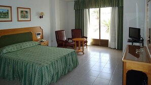 Una camera d'albergo con un letto, due poltrone, una scrivania con televisore e una finestra con tende.