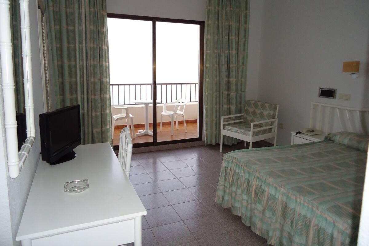 Une chambre d’hôtel comprenant un lit, un bureau avec une télévision, une chaise et un balcon avec une table et des chaises.