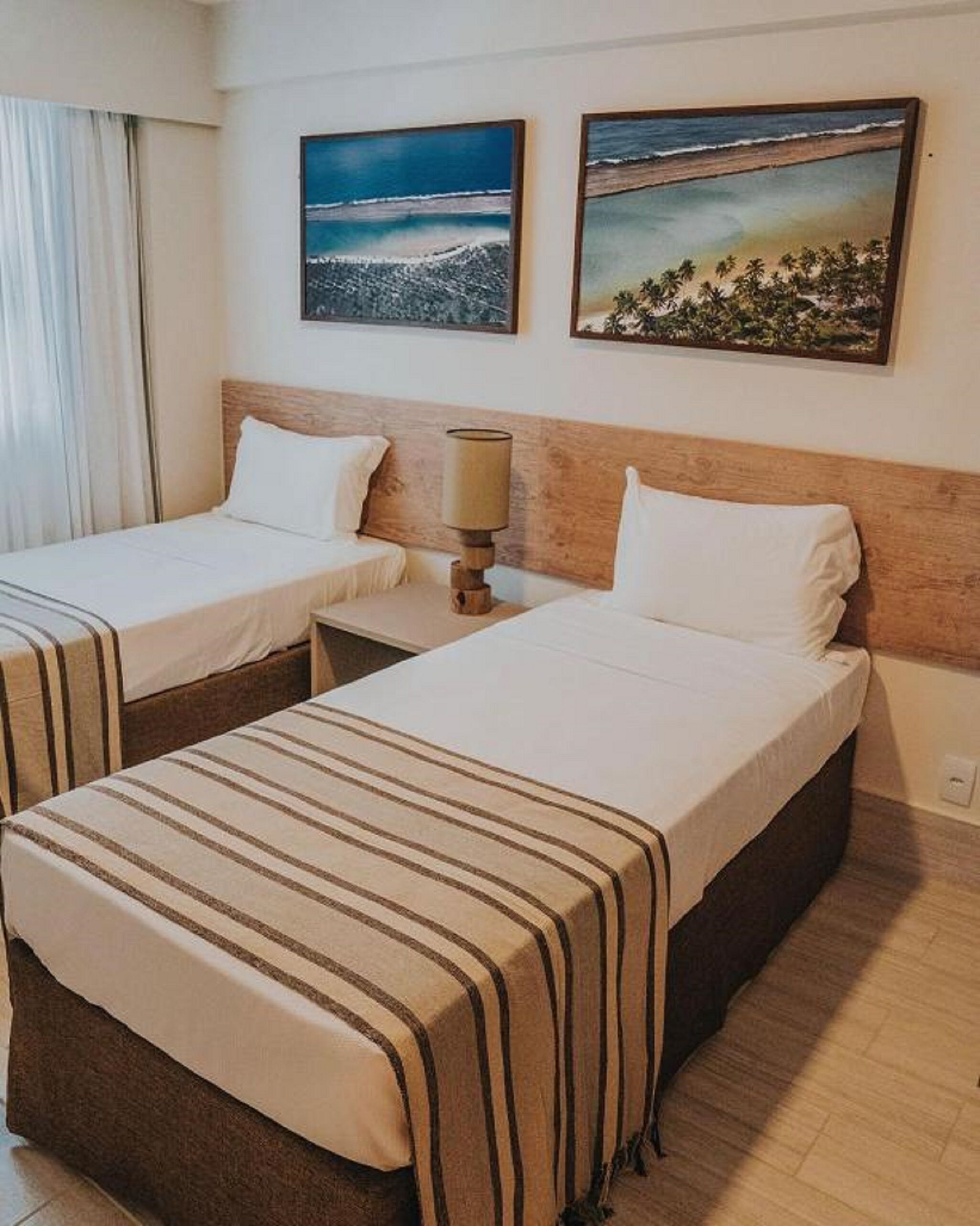 A hotel room with two beds, a nightstand with a lamp, and two framed pictures on the wall.
