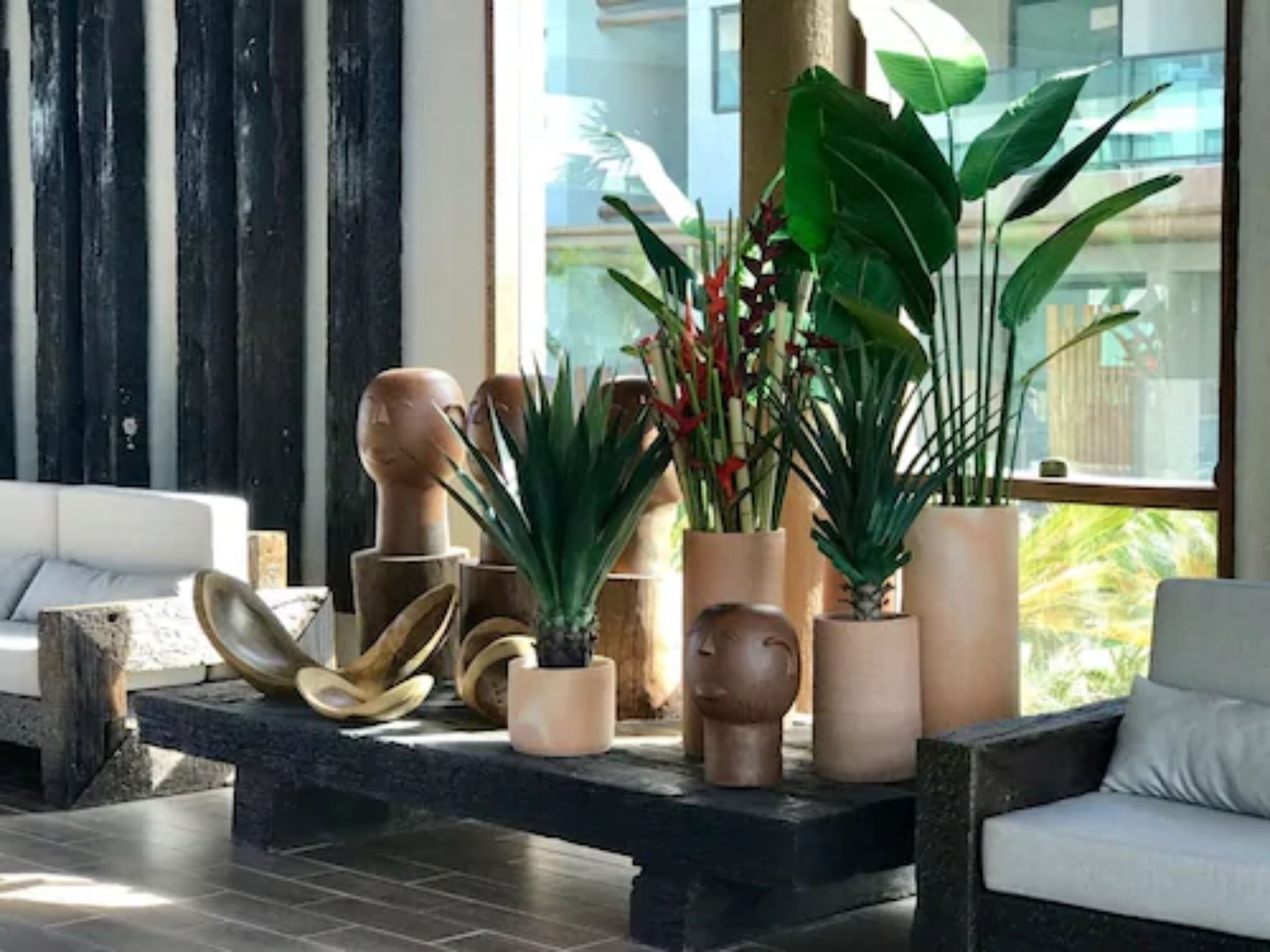 A modern living room with a sofa, a coffee table with decorative items, and large windows with a view of greenery.