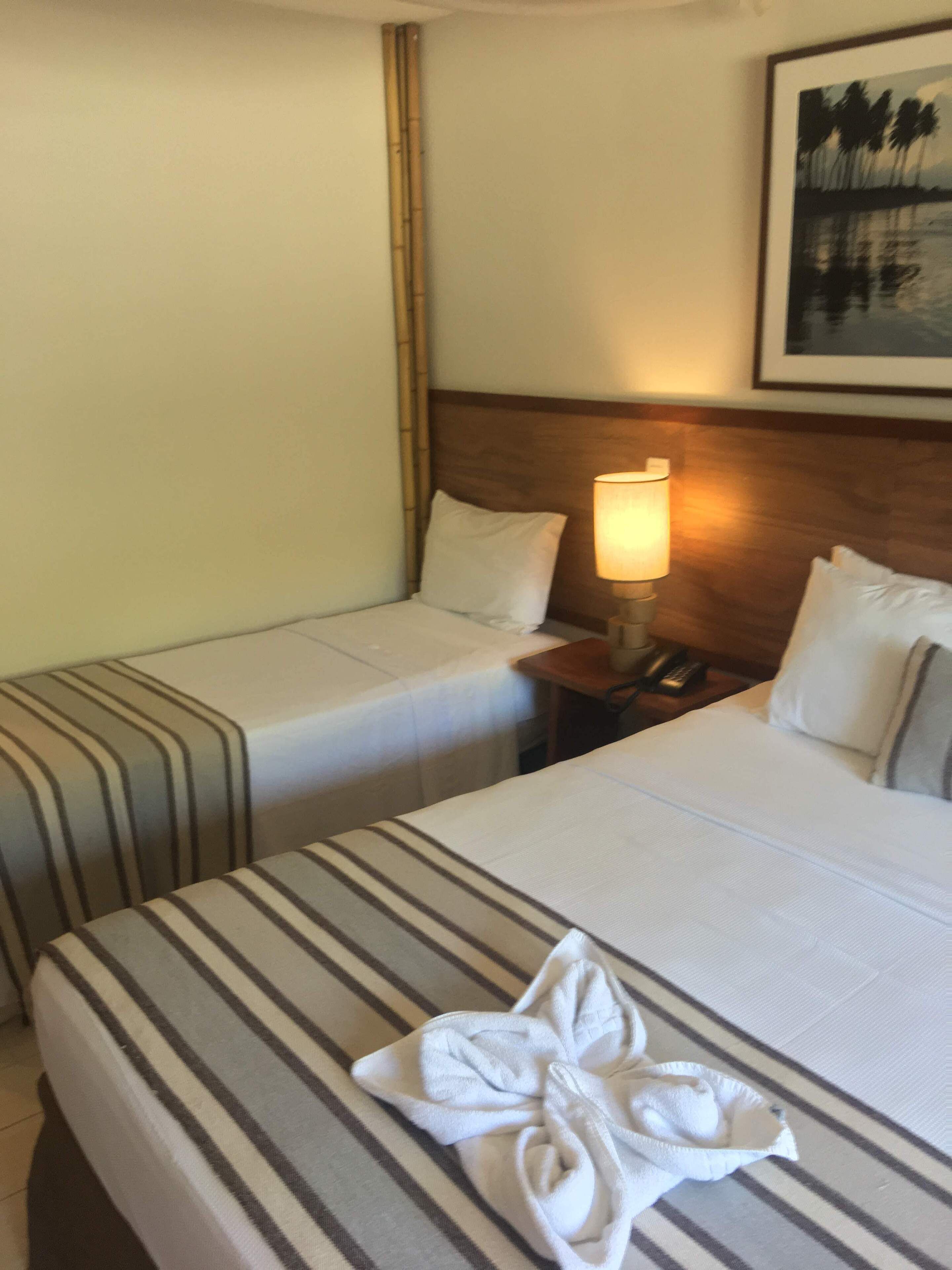 A hotel room with two single beds, a nightstand with a lamp, and a painting on the wall.
