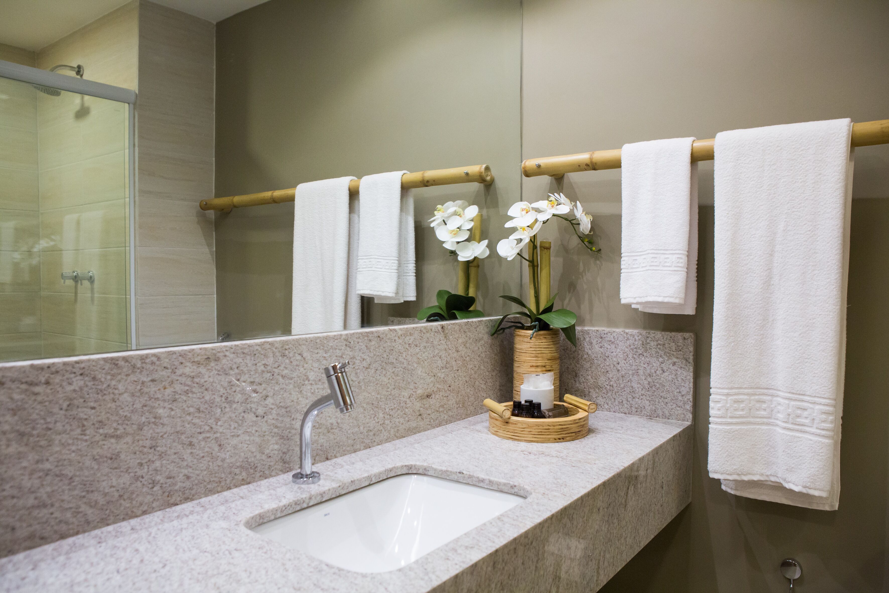 A bathroom with a granite countertop, a sink, a mirror, and a towel rack with white towels.