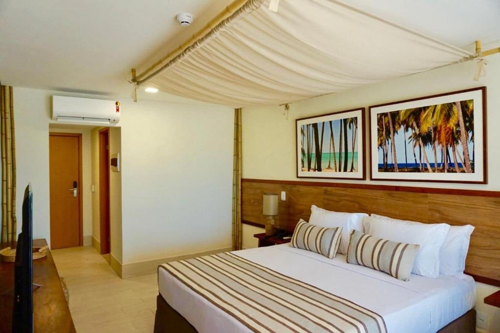 A hotel room with a bed, a television, an air conditioning unit, and framed pictures on the wall.