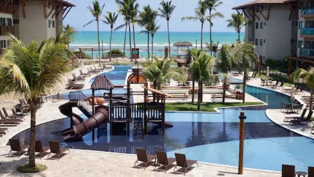 A resort pool area with palm trees, lounge chairs, and a view of the beach. - Samoa Beach Resort (Ipojuca)