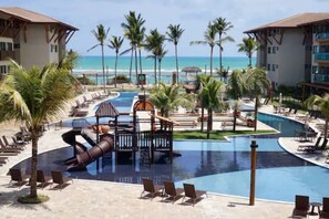 A resort pool area with palm trees, lounge chairs, and a view of the beach.