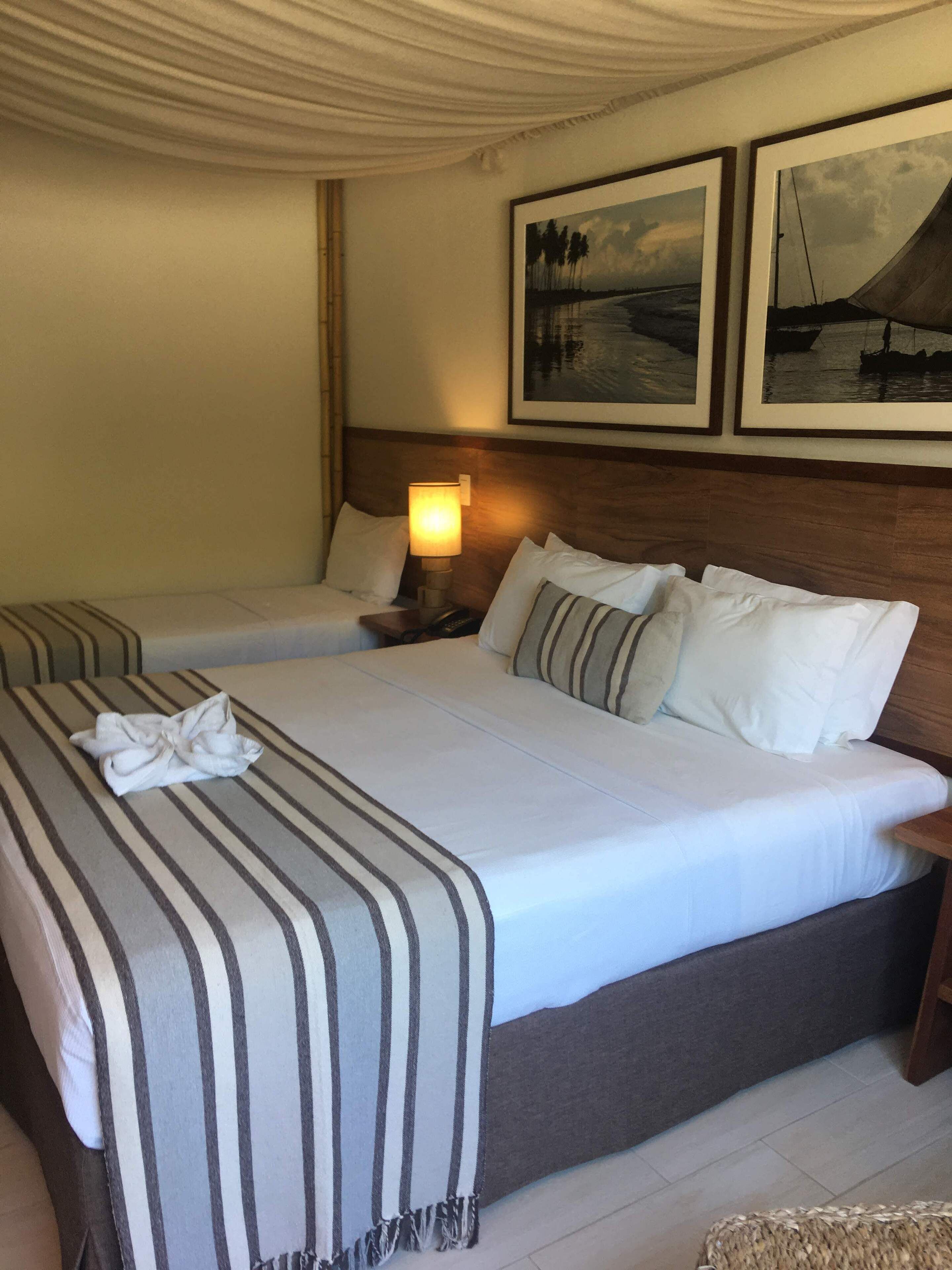 Una habitación de hotel con dos camas, una mesita de noche con lámpara y dos cuadros enmarcados en la pared.