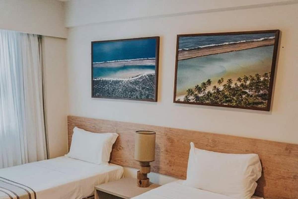 Habitación de hotel con dos camas, una mesita de noche con lámpara y dos cuadros en la pared.