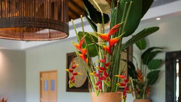 A reception area with a wooden counter, a large vase with tropical flowers, and a woven light fixture.