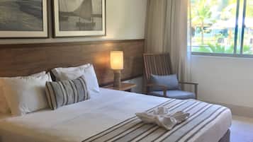 A hotel room with a large bed, a nightstand with a lamp, a chair, and two framed pictures on the wall.