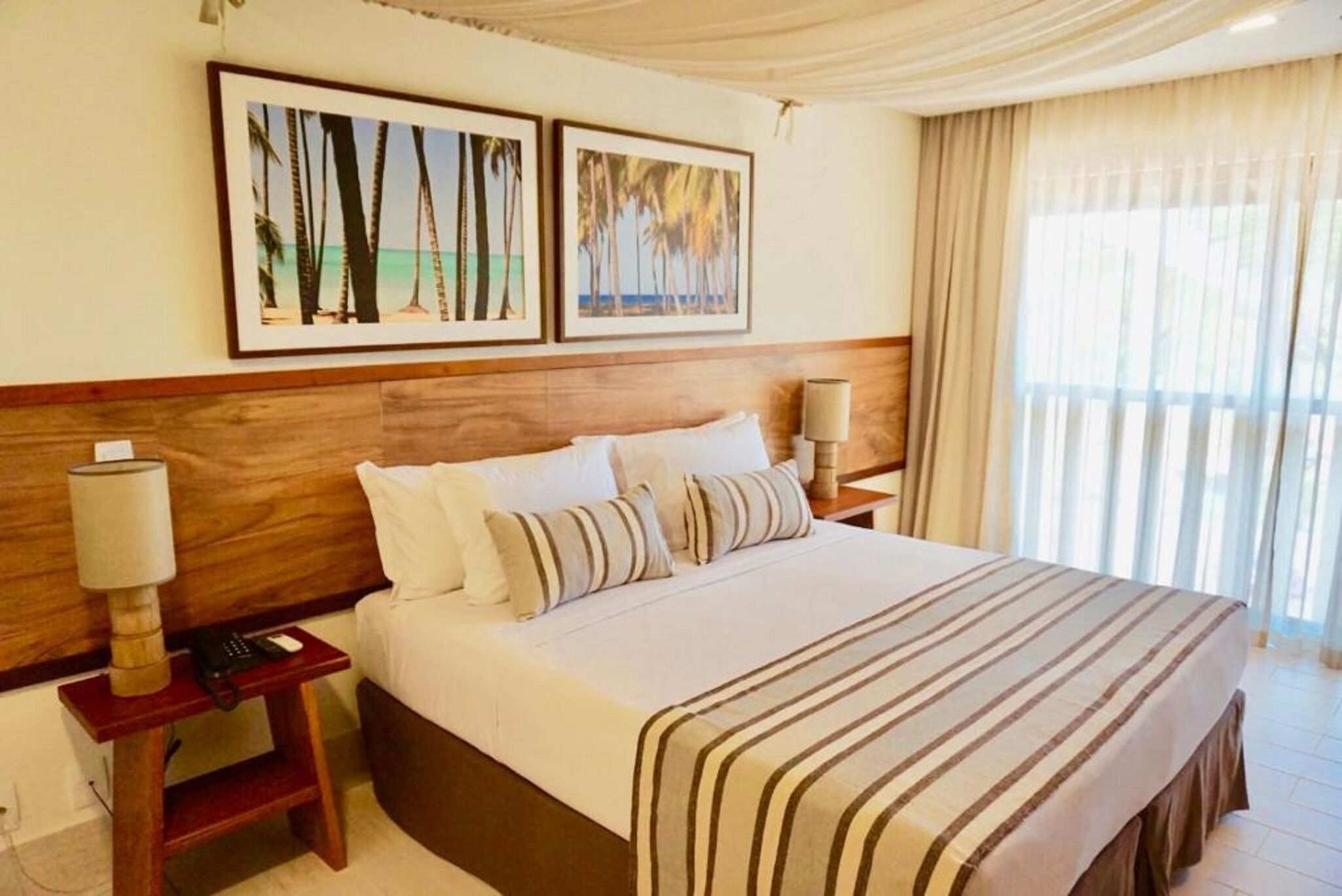 A hotel room with a large bed, two bedside tables, a wooden headboard, and framed pictures on the wall.
