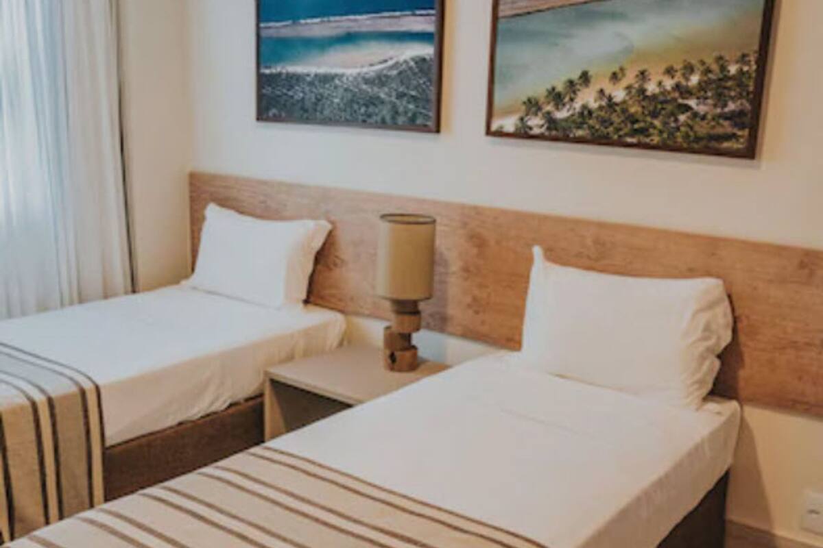 A hotel room with two single beds, a nightstand with a lamp, and two framed pictures on the wall.